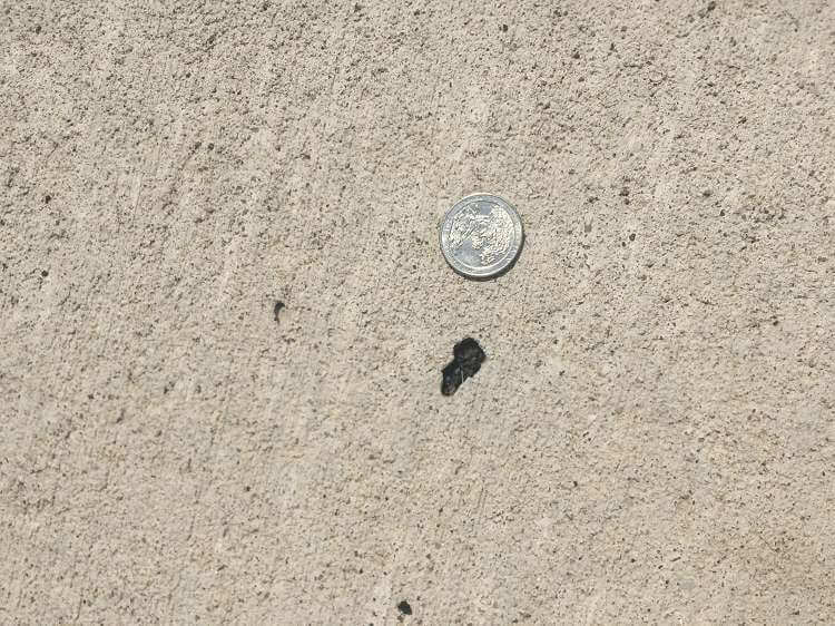 A closeup of concrete with a small hole next to a silver quarter.