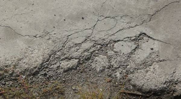 A closeup view of old cement that is beginning to erode and break away into pieces of gravel and different cracks.
